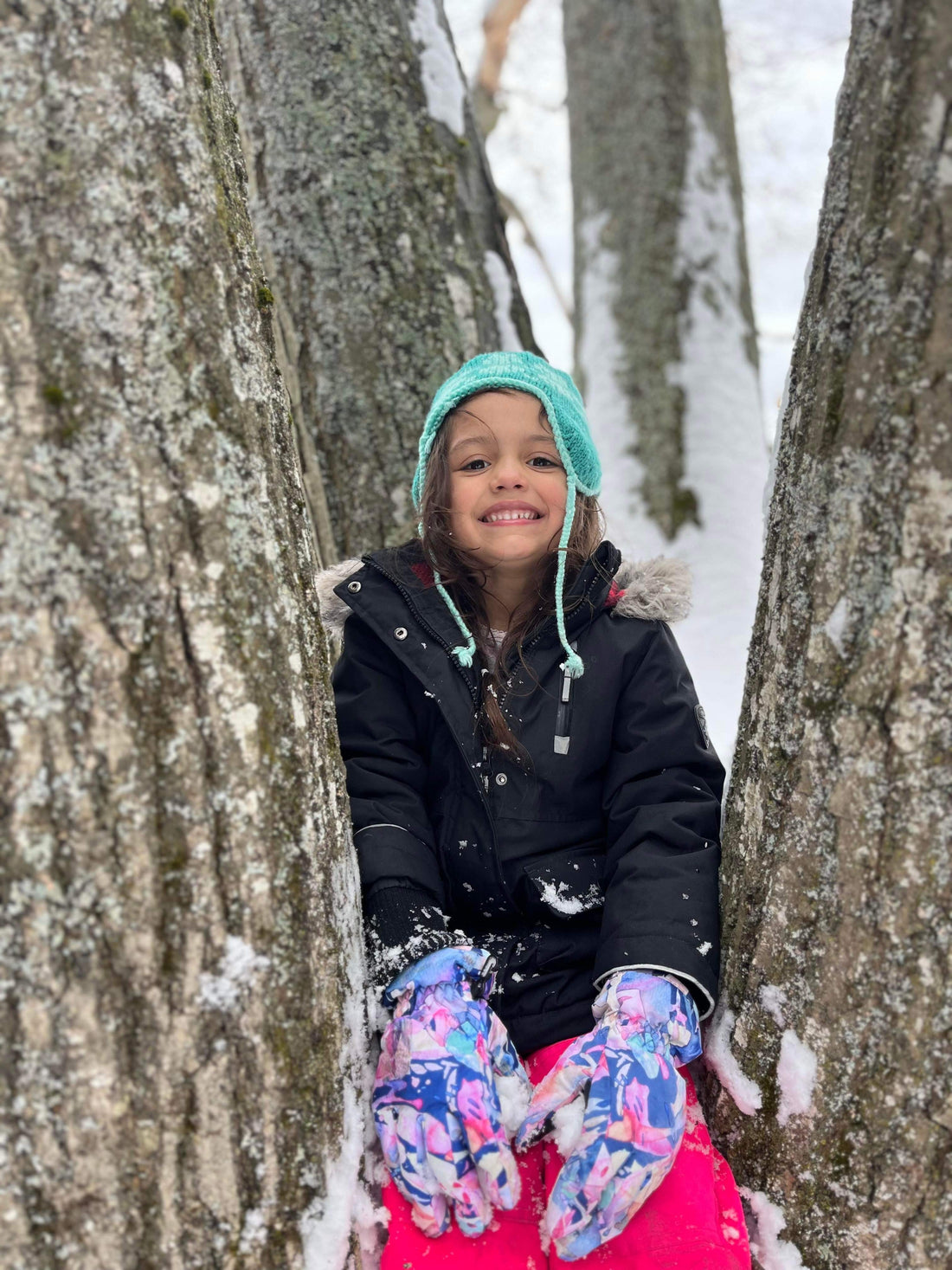 Picture of a child wearing winter outerwear sitting in a snowy tree 